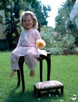 Smiling girl sitting on a chiar on the lawn with a yellow flower