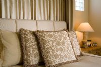 Detail of neutral toned decorative pillows on bed with lamp.