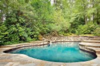 View of pool with stone patio and greenery