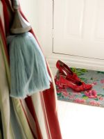 Red shoes on door mat. Striped curtains with tassel in foreground
