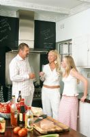 Three people talking in kitchen holding champagne glasses