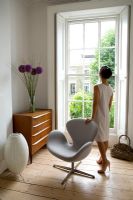 Woman standing next to Arne Jacobsen 'Swan' chair looking out of window