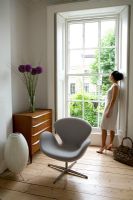 Woman looking out of window. Arne Jacobsen 'Swan' chair in foreground.