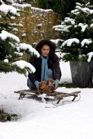 Woman putting logs on sledge in snowy garden