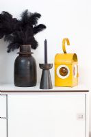 Black vase with feathers, candlestick and lantern on cabinet