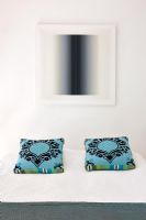 Turquoise patterned cushions on bed under artwork