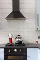 Black cooker and extractor hood with white tiled wall