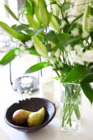Pears in bowl next to vase of flowers