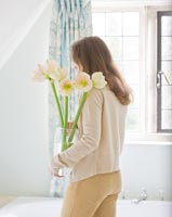 Woman holding vase of Amaryllis 'Cherry Blossom'  in  bathroom