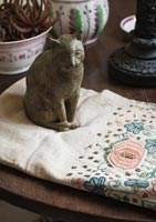 Cat sculpture sitting on embroidered fabric
