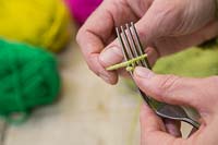 Making christmas pompom decorations from wool - Hold one end of the wool in place with one finger and begin to wrap the wool around the fork