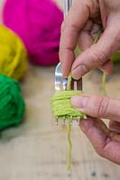 Making christmas pompom decorations - Cut a separate length of wool and thread this through the gap of the middle prong on the fork 