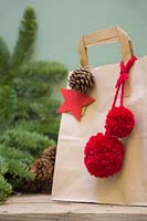 Brown paper christmas gift bag decorated with pine cone, felt star and wool pompoms