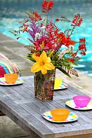 Vase of Crocosmia and Daylily flowers on garden table