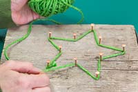 Making a christmas star decoration - Weave the green wool between the copper nails to recreate the star shape