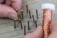 Making copper wire star decorations - Weave the copper wire around the nails to form a star 