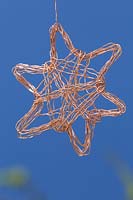 Making copper wire stars - finished decorations hanging  against a blue background