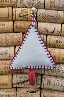 Making stitched felt christmas decorations - miniature christmas tree made from felt and decorative string, hanging against a wine cork board