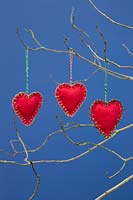 Red hearts stitched together with felt fabric, hanging from twigs