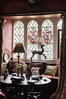 Window seat with cushions showing antique stump work and stained glass window - Cothay Manor