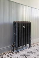 Cast iron radiator against wooden panel and tiled floor