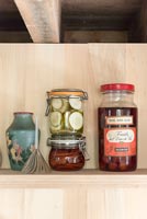 Jars of pickles and objects on shelves beneath exposed wooden beams