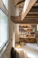 Shelves and log store in narrow living room with exposed wooden beams