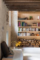 Wooden shelves and log store in living room with exposed beams 
