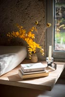 Modern wooden side table with books and autumnal arrangement in vase by window