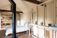 Modern open plan bedroom with wooden walls and exposed flue 