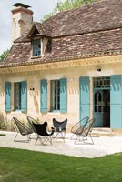 Turquoise shutters and modern black chairs outside country house 