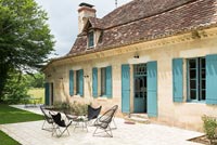 Country house exterior with turquoise painted shutters and black chairs 