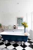 Blue free standing rolltop bath in bathroom with black and white floor 