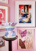 Framed photographs and paintings on pink wall with colourful pottery 