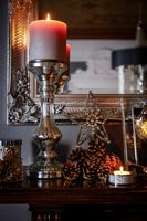 Christmas decorations and lit candle on mantelpiece 