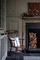 Wooden armchair next to log store in fireplace 