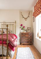 Country bedroom with wall mounted antlers and wooden chest of drawers 