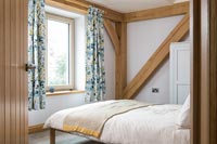 Single guest bedroom with exposed wooden beams and floral curtains 