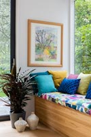 Framed painting above colourful cushions on window seat 
