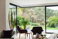 Armchairs facing glazed living room wall with views to woodland garden 