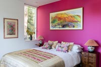 Vivid pink feature wall and colourful artwork in modern bedroom 