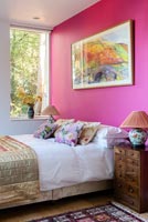 Vivid pink painted wall and artwork in modern bedroom 