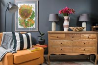 Orange leather chair and wooden sideboard in living room with dark grey walls 