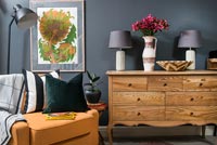 Orange leather chair and wooden sideboard in living room with dark grey walls 