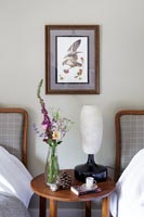 Wooden bedside table with lamp and flowers in country bedroom 