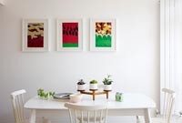 Colourful paintings on wall of white dining room 