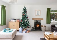 Christmas tree in modern living room with lit wood burning stove 