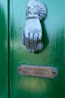 Hand shaped door knocker and plaque on green painted front door  