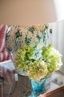 Lime green cut flowers in vase by lamp on side table 
