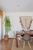 Modern dining room with fabric wall hanging and large houseplant 